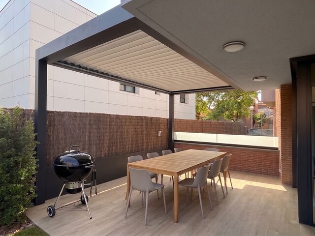 Pérgola bioclimática CERCA ampliando el porche existente de una vivienda, a última hora de la tarde