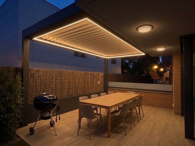 Pérgola bioclimática CERCA ampliando el porche existente de una vivienda, de noche, con la iluminación LED encendida