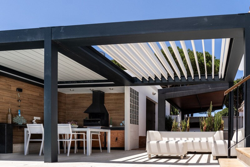 Pérgola bioclimática retráctil CERCA con las lamas abiertas al 80% sobre una terraza con piscina y cocina exterior